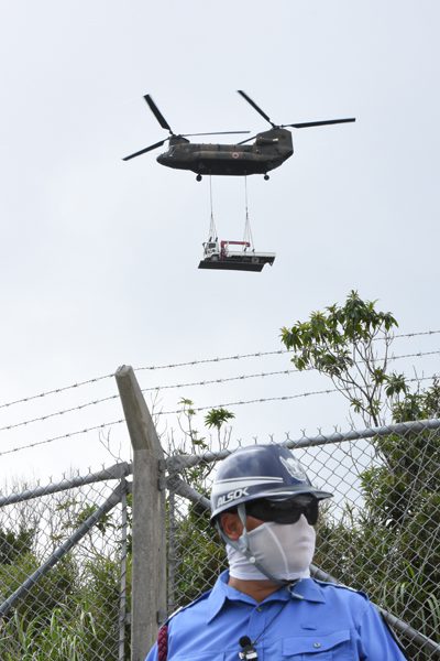 政府は米軍基地建設のため自衛隊ヘリまで動員した。資機材をつり下げたまま、県道の上を飛んだ＝2016年9月13日、東村高江、撮影・阿部岳