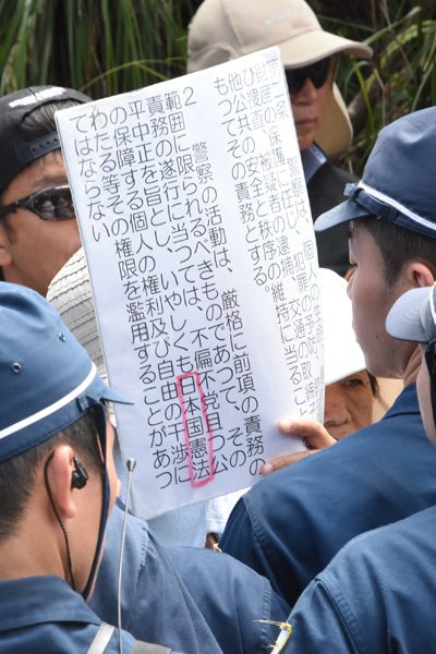 警察法2条をプラカードにして警官に示す市民。「日本国憲法」の文字が強調されていた＝2016年9月21日、国頭・東の村境、撮影・阿部岳