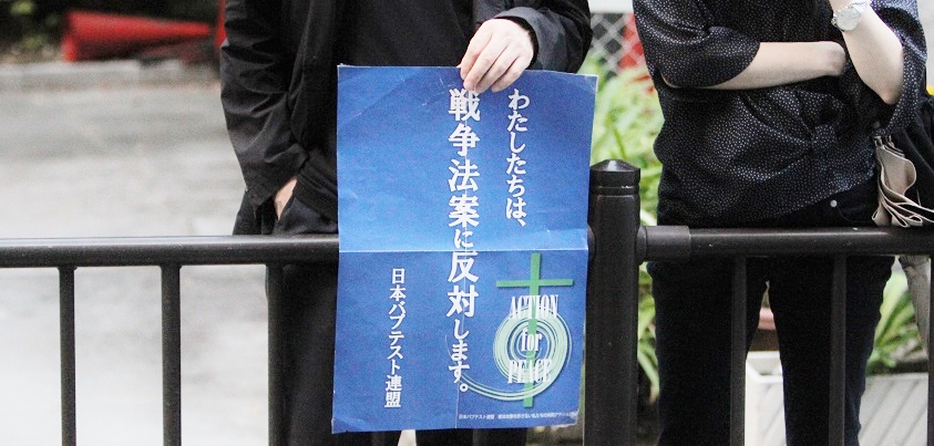 安保法案反対のデモ行進が進む沿道で「わたしたちは、戦争法案に反対します。」と書かれた日本バプテスト連盟のポスターを掲げる人＝２０１５年９月１３日、大阪市内で、撮影・橋本正人