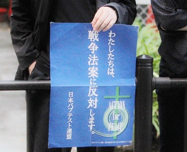 安保法案反対のデモ行進が進む沿道で「わたしたちは、戦争法案に反対します。」と書かれた日本バプテスト連盟のポスターを掲げる人＝２０１５年９月１３日、大阪市内で、撮影・橋本正人