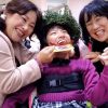 一足早くハーブの冠を被り、クッキーのメダルをかけたレノアちゃん　右はPASの野村寿子さん　左はお母さんの敦子さん＝撮影・松中みどり