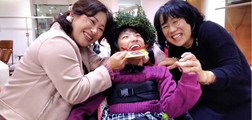 一足早くハーブの冠を被り、クッキーのメダルをかけたレノアちゃん　右はPASの野村寿子さん　左はお母さんの敦子さん＝撮影・松中みどり